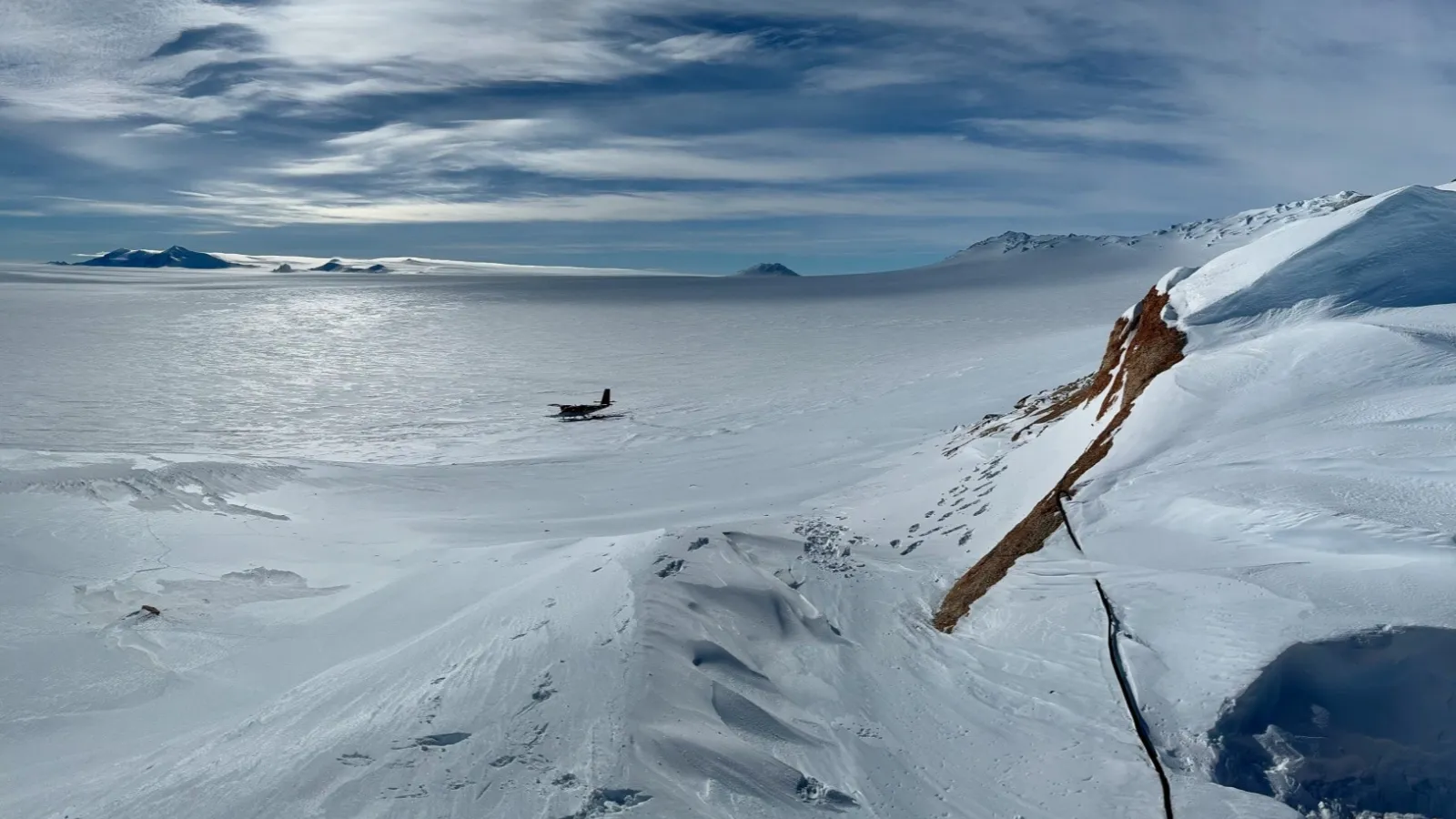 a view from a glacier, overlooking an ice field with a small plane