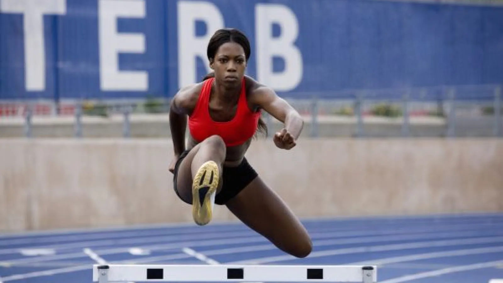 a young black woman running hurdles on a college track