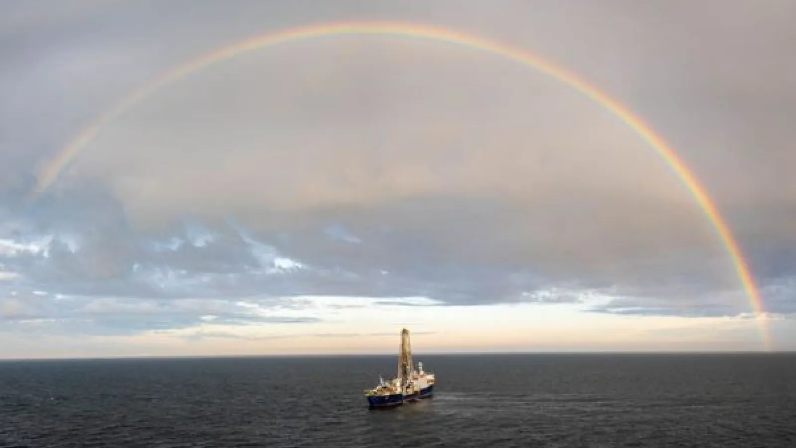 a research ship on the open ocean, below a rainbow