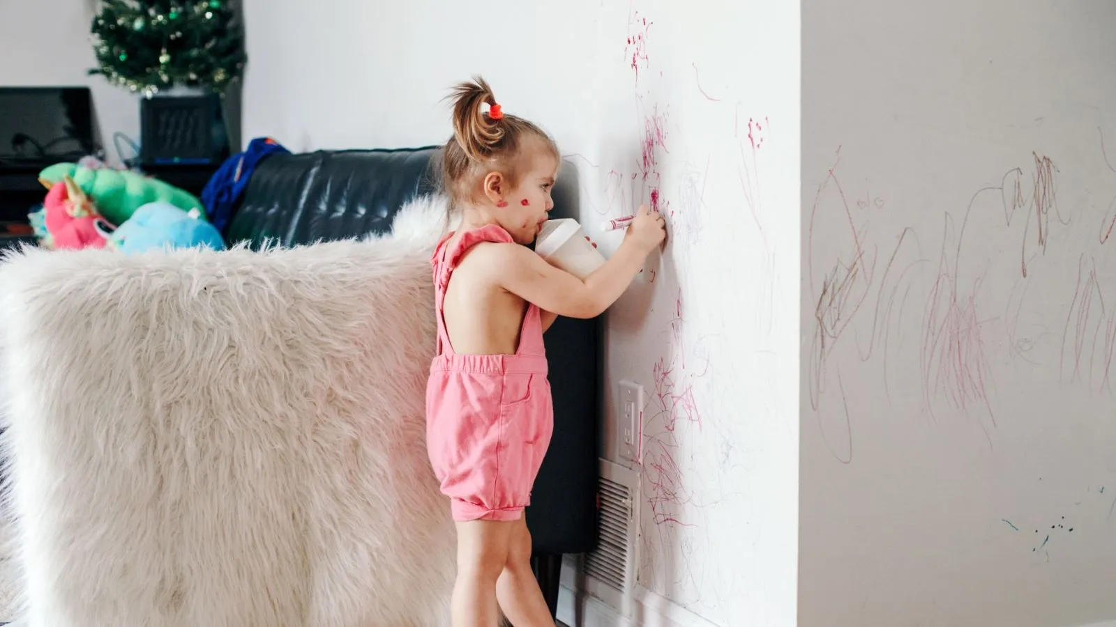 a toddler drawing on a wall with red crayon