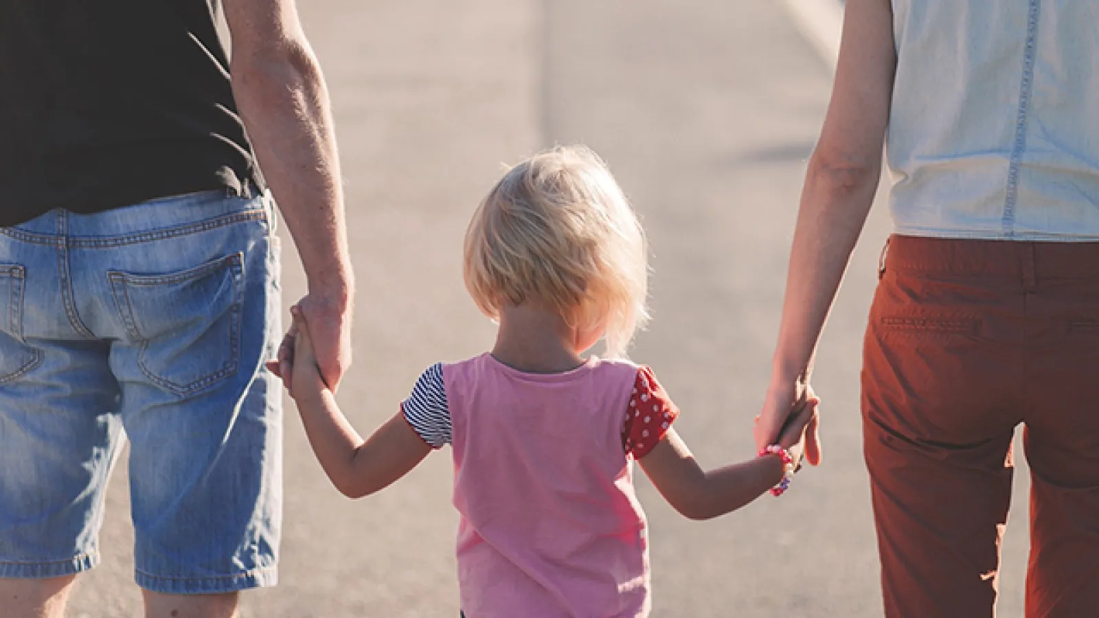 Parents hold hands with their young child on a beach